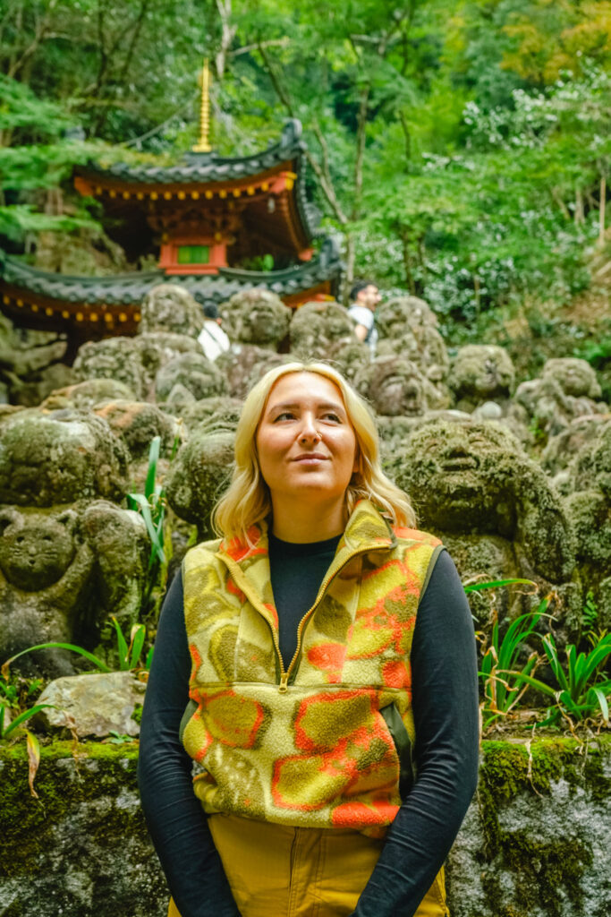 blonde woman stands in front of moss covered Arhat statues at Otagi Nenbutsu-ji Temple in Kyoto